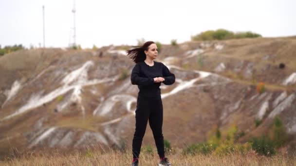 若い女性の暖かい丘陵地帯でアップを行う 大人女性で黒カジュアル服行うスポーツで新鮮な空気で田舎 — ストック動画