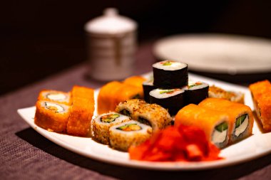 Kafedeki beyaz tabakta iştah açıcı suşi servisi. Geleneksel Japon restoranında wasabi ve zencefilli lezzetli suşi rulolarını kapatın.