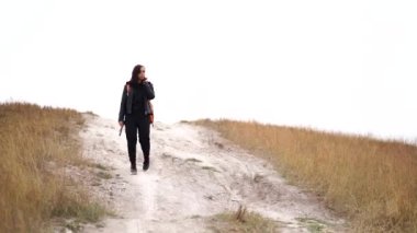 Sırt çantalı genç bir kadın bulutlu bir havada tepeden iniyor. Kırsal kesimdeki tebeşir dağında yürüyen kadın turist.