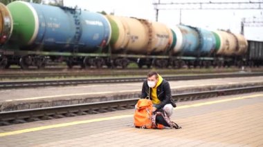 Genç adam platformda duruyor, treni bekliyor. Demiryolu platformunda sırt çantalı bir erkek yolcu tren yolculuğu için bekliyor. Turizm, seyahat ve dinlenme kavramı