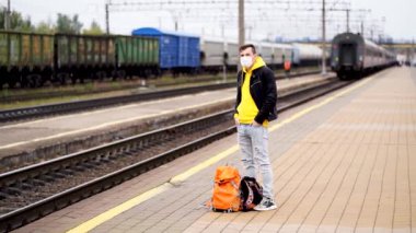 Genç adam platformda duruyor, treni bekliyor. Demiryolu platformunda sırt çantalı bir erkek yolcu tren yolculuğu için bekliyor. Turizm, seyahat ve dinlenme kavramı