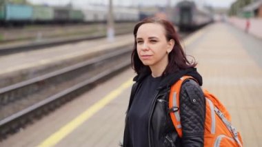 Genç bir kadın platformda duruyor, treni bekliyor. Tren yolu platformunda sırt çantalı kadın yolcu portresi. Turizm, seyahat ve dinlenme kavramı