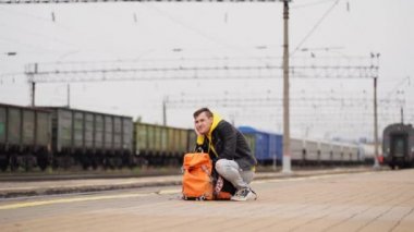 Genç adam platformda duruyor, treni bekliyor. Demiryolu platformunda sırt çantalı bir erkek yolcu tren yolculuğu için bekliyor. Turizm, seyahat ve dinlenme kavramı