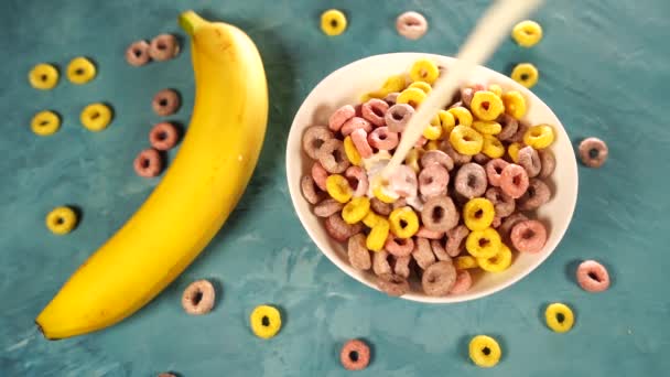 Hälsosam frukost med spannmål och banan. Från ovan av skål med läcker hälsosam frukost gjord med färgglada spannmål ringar och banan med mjölk serveras på blått bord — Stockvideo