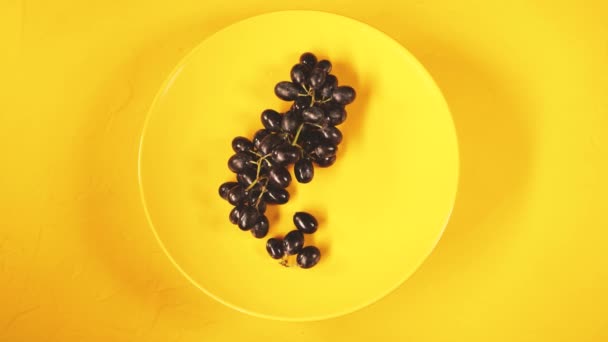 Černé hrozny na žlutém talíři. Zralé hrozny na žlutém texturovaném pozadí. Koncept: ovoce a zdravé potraviny — Stock video