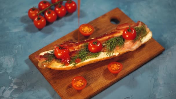 Stilleven van smakelijke bruschetta op houten plank. Close-up van sandwich met gesmolten kaas, spek, kerstomaten, dille en saus op blauwe achtergrond. — Stockvideo