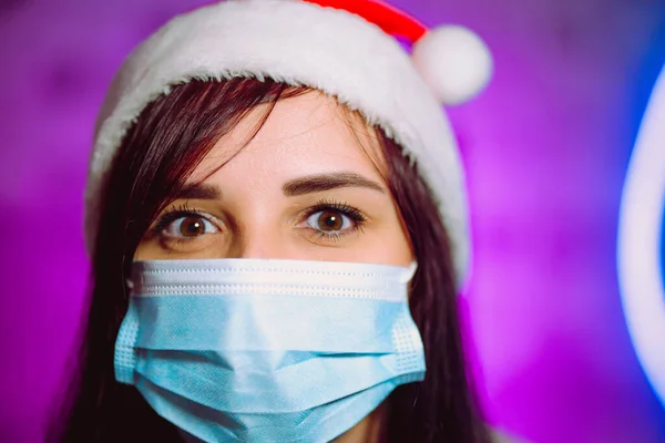 Молодая Женщина Медицинской Маске Шляпе Санта Клауса Против Освещенной Стены — стоковое фото