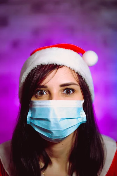 Молодая Женщина Медицинской Маске Шляпе Санта Клауса Против Освещенной Стены — стоковое фото