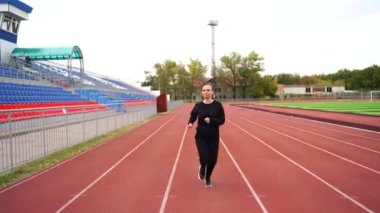 Stadyumda temiz havada koşan genç aktif bir kadın. Açık hava stadyumunda kırmızı pist üzerinde koşan yetişkin bir kadın spor giysisi. Sağlıklı yaşam tarzı kavramı.