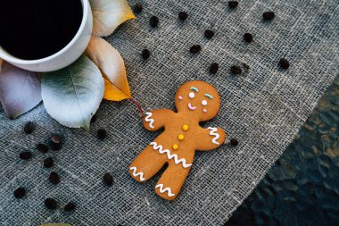 Zencefilli çörek adam ve sonbahar yapraklarının yanında bir fincan kahve. Tatlı zencefilli adam ve koyu espresso kahvesinin üst görüntüsü. Renkli sonbahar yapraklarının yanına koyulmuş keten kumaş örtüsü.