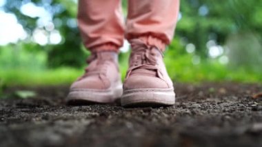 Ayaklarını yere basan ayakkabılarla kapat. Pembe spor ayakkabılı kadın yazın parkta durur..