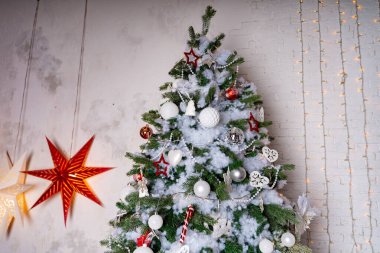 Odada süslü bir Noel ağacı var. Bayram kutlamaları sırasında beyaz duvarın yanında beyaz ve kırmızı mücevherleri olan kozalaklı ağaçlar..