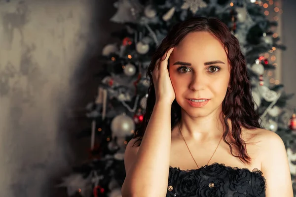 圣诞树附近穿着黑色衣服的迷人的黑发画像 年轻迷人的女子在针叶树前摆姿势 装饰着装饰品 在家里庆祝圣诞节的概念 — 图库照片