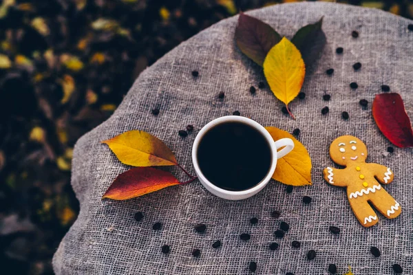 Gingerbread man and cup of coffee near autumn leaves. Top view of sweet gingerbread man and cup of strong espresso coffee placed near colorful autumn leaves on linen cloth in park