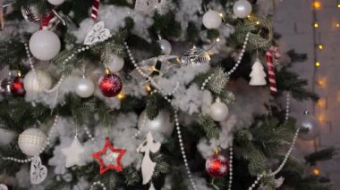 Odada süslü bir Noel ağacı var. Bayram kutlamaları sırasında beyaz duvarın yanında beyaz ve kırmızı mücevherleri olan kozalaklı ağaçlar.