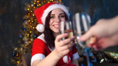 Noel Baba kostümlü genç bir kadın şampanya bardaklarına vurup Noel ağacının yanındaki sandalyeye oturuyor. Çekici esmer gülüşler ve kabarcıklı içkiler. Evde Noel kutlaması kavramı