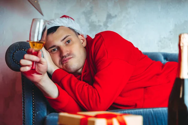 모자를 샴페인을 마시고 소파에 젊은이 수컷이 방에서 있습니다 가정에서의 크리스마스 — 스톡 사진