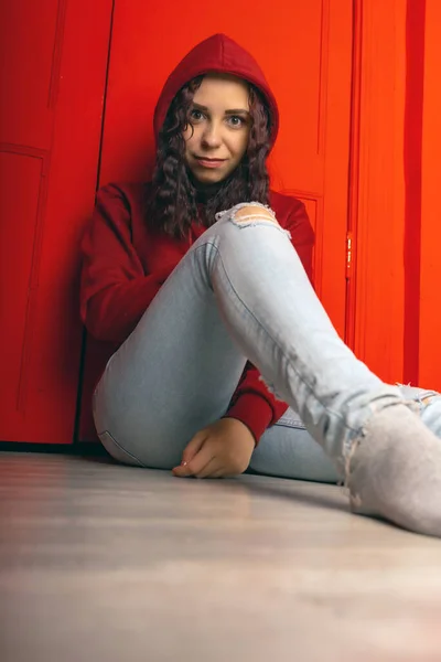 Młoda Kobieta Kapturze Siedzi Podłodze Kręcone Brunetka Stanowi Pobliżu Czerwonej — Zdjęcie stockowe