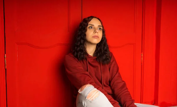 Genç Bir Kadın Yerde Oturuyor Kıvırcık Esmer Kırmızı Duvarın Yanında — Stok fotoğraf