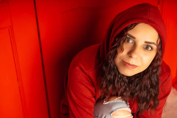 Kapüşonlu Genç Bir Kadın Yerde Oturuyor Kıvırcık Esmer Kırmızı Duvarın — Stok fotoğraf