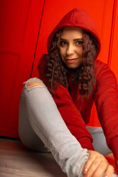 Jovem Capuz Sentada Chão Curly Morena Posa Perto Parede Vermelha — Fotografia de Stock