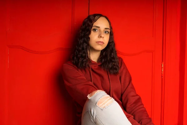 Mladá Žena Sedící Podlaze Kudrnatá Bruneta Pózuje Blízko Červené Stěny — Stock fotografie
