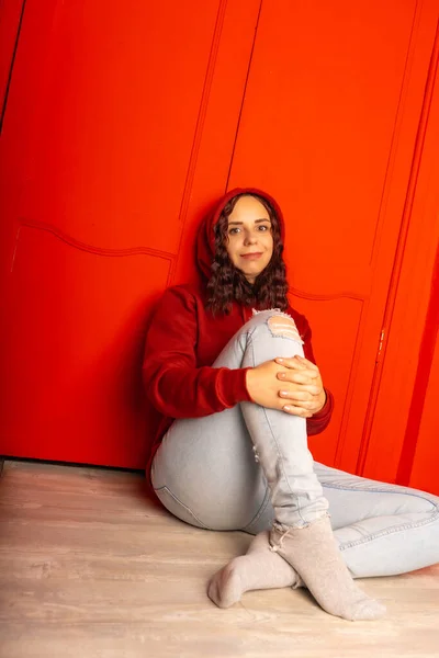 Mladá Žena Kapuci Sedí Podlaze Kudrnatá Bruneta Pózuje Blízko Červené — Stock fotografie