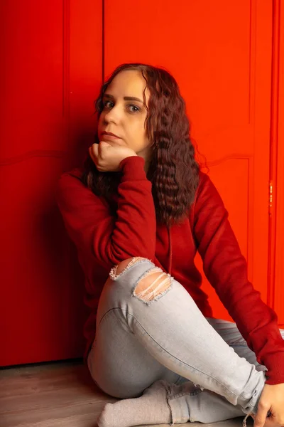 Молода Жінка Сидить Підлозі Кучерявий Брюнетка Позує Біля Червоної Стіни — стокове фото