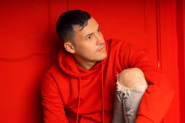 Genç yakışıklı erkek yerde oturuyor. Düşünceli adam kırmızı duvarın yanında poz veriyor.