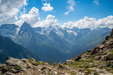 Bulutlu gökyüzüne karşı karlı dağ. Beyaz bulutların altından mavi gökyüzünde yüzen dağların üzerinden doğada güneşli bir günde karla kaplı..