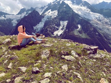 Dağın tepesinde oturan kadının yan görüntüsü. Dişi turistler güneşli havalarda güzel dağların tadını çıkarırlar.