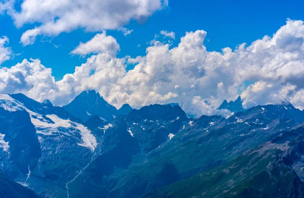 Bulutlu gökyüzüne karşı karlı dağ. Beyaz bulutların altından mavi gökyüzünde yüzen dağların üzerinden doğada güneşli bir günde karla kaplı..