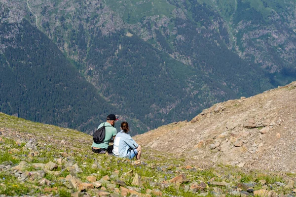 Kayaların üzerinde oturan ve dağlarda dinlenen kadın ve erkeğin arka görüntüsü. Evli çift güneşli havalarda güzel dağların tadını çıkarırlar.