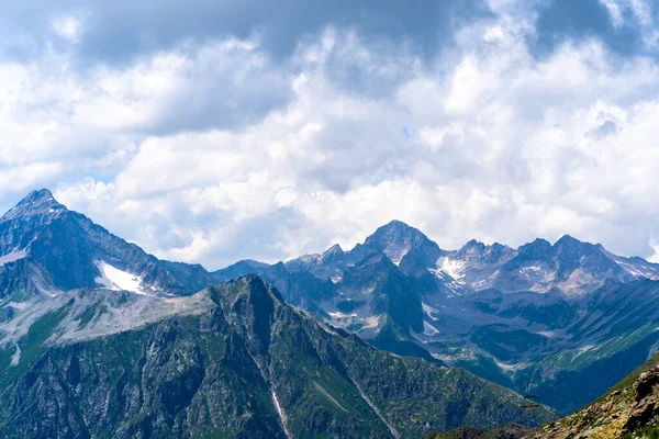 Bulutlu gökyüzüne karşı karlı dağ. Beyaz bulutların altından mavi gökyüzünde yüzen dağların üzerinden doğada güneşli bir günde karla kaplı..