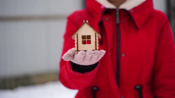 小さな木の家と冬に親指を示す他の手を保持手袋で一人の女性の手の閉じる 新しいアパートの購入の概念 — ストック動画