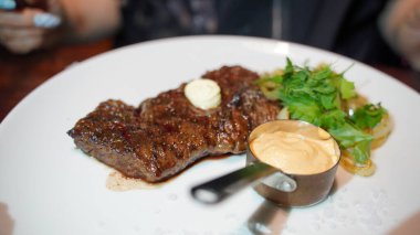 Sos ve sebzeli sulu bifteği beyaz tabakta yakın. Lokantada kızartılmış soğan ve yeşillik ile iştah açıcı et yemeği.