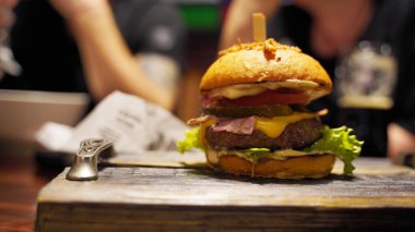 Kafedeki tahta tahtada sulu burger yakın çekim. Sebzeli, peynirli, pastırmalı ve soslu iştah açıcı hamburger.