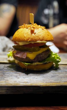 Kafedeki tahta tahtada sulu burger yakın çekim. Sebzeli, peynirli, pastırmalı ve soslu iştah açıcı hamburger.