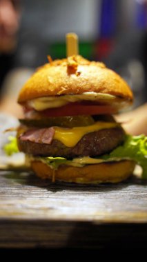 Kafedeki tahta tahtada sulu burger yakın çekim. Sebzeli, peynirli, pastırmalı ve soslu iştah açıcı hamburger.