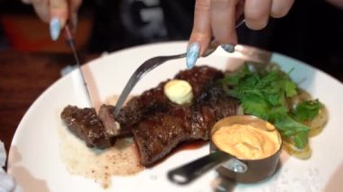 Kadınların ellerini kapayın, leziz biftekleri kesin ve sosu serpin. Tanınmayan kişi restoranda yemek yiyor..