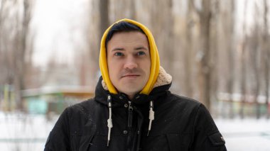 Kışın sokakta sarı başlıklı genç adamın portresi. Yetişkin bir erkeğin kış mevsiminde yürüyüş yaparken poz vermesine yakın.