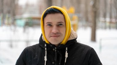 Kışın sokakta sarı başlıklı genç adamın portresi. Yetişkin bir erkeğin kış mevsiminde yürüyüş yaparken poz vermesine yakın.