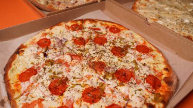 Turuncu arka plandaki büyük pizza kutularını kapatın. Farklı malzemelerle iştah açıcı pizzalar..