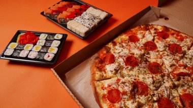 Konteynırlarda iştah açıcı suşi ve turuncu arka planda büyük boy pizza. Pizza ve farklı malzemelerle lezzetli suşi ruloları.