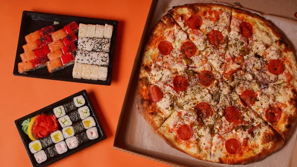 Konteynırlarda iştah açıcı suşi ve turuncu arka planda büyük boy pizza. Pizza ve farklı malzemelerle lezzetli suşi ruloları.