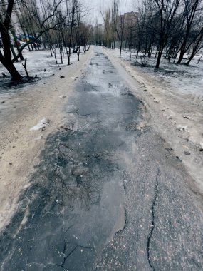 Bahar mevsiminde su birikintileriyle yürüme yolunu kapatın. Erimiş kar ve kenarlarında kirli karla mahvolmuş bir yol.
