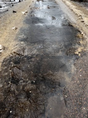 Bahar mevsiminde su birikintileriyle yürüme yolunu kapatın. Erimiş kar ve kenarlarında kirli karla mahvolmuş bir yol.
