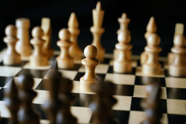 Gemideki beyaz ve siyah satranç taşlarını kapatın. Satranç tahtasındaki beyaz piyonun ilk hamlesine odaklan. Akıllı, mantıklı ve stratejik oyun kavramı