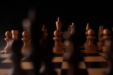 Gemideki siyah satranç taşlarını kapatın. Siyah arka planda satranç tahtasında iki sıra tahta figür. Akıllı, mantıklı ve stratejik oyun kavramı.