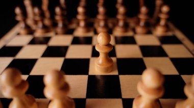 Gemideki beyaz ve siyah satranç taşlarını kapatın. Satranç tahtasındaki beyaz piyonun ilk hamlesine odaklan. Akıllı, mantıklı ve stratejik oyun kavramı